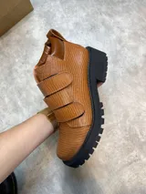 Borcegos de cuero color marrón con textura tipo reptil, caña baja, ajuste con dos correas con hebilla y suela track color negro.