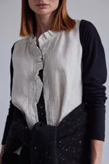 Blusa de estilo romántico con frente de lino y espalda y mangas de algodón con elastano. Presenta un diseño con mini volados en la pechera, cuello redondo y cierre frontal con botones.