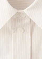 Camisa de algodón color crudo, con cuello camisero, botonadura frontal y mangas largas.