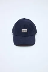 Gorra de pana azul marino con visera curva, parche frontal con texto y pequeño bordado rojo en el lateral.