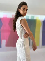 Mono largo color blanco, de lino con algodón, con bordado texturizado en los laterales superiores, cinto para ajustar en la cintura, cierre invisible central y bolsillos laterales.