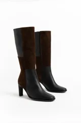 Botas altas bicolor de caña recta, confeccionadas en una combinación de paneles de cuero negro y gamuza marrón. Presentan punta cuadrada suave, cierre lateral interno y taco fino.