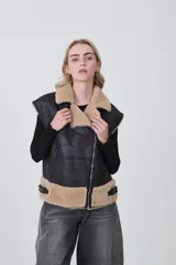 Chaleco sin mangas de cuero sintético negro con interior y detalles de piel sintética en color beige. Presenta cierre frontal asimétrico, cuello solapa y correas ajustables en la cintura.