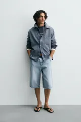 Bermuda de denim de algodón, color celeste claro lavado, de corte ancho (relaxed fit) y largo hasta la rodilla. Presenta cierre frontal con botón y cremallera, bolsillos delanteros y bolsillos traseros de plastrón.