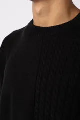 Sweater negro de calce relajado con diseño de textura combinada, presentando un lado liso y otro con tejido de ochos. Cuenta con cuello redondo y una etiqueta decorativa en el frente.