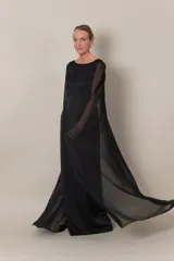 Vestido largo de crepe negro, con capa de gasa que sale de los hombros y abertura en la espalda.