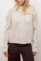 Buzo de punto color beige con cuello redondo, mangas largas con flecos decorativos y diseño de trenzas en el frente.