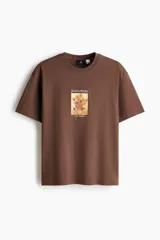 Remera marrón de algodón con cuello redondo, mangas cortas y hombros caídos, de corte holgado. Presenta un estampado frontal con la obra 'Los girasoles' de Van Gogh y el texto 'Sunflowers' en la parte superior y '-Van Gogh-' en la inferior.