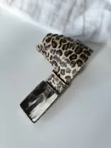 Cinto de cuero con estampado animal print y hebilla rectangular con diseño abstracto en blanco y negro.