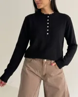 Sweater de punto negro con cuello redondo, cierre frontal parcial con botones y detalle de borde ondulado en la tapeta.