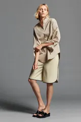Camisa oversize color beige con mezcla de algodón, cuello smoking, manga larga con puños anchos y cierre frontal con botones ocultos por solapa.