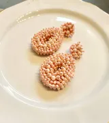 Aros colgantes con forma de gota y de botón, recubiertos de pequeñas cuentas rosadas.