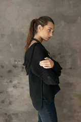 Sweater de punto negro con capucha, diseño de manga larga y corte holgado. Presenta un detalle de argolla metálica en el escote.