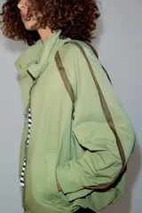 Cazadora ZARA Woman Collection color verde militar, con cuello alto, manga larga y bolsillos frontales. Cuenta con detalles de vivos a contraste en los hombros, bajo elástico asimétrico y cierre frontal oculto con cremallera y botones.
