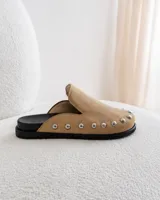 Zuecos de ante color beige con diseño destalonado, punta redonda y tachas metálicas plateadas alrededor de la suela.