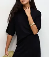 Blusa de punto de corte holgado, color negro, con cuello redondo elevado y mangas cortas amplias con sisa desplazada.