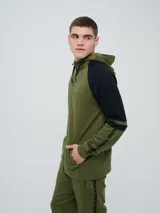 Campera canguro deportiva Umbro para hombre, de color verde militar con mangas negras de diseño raglán y detalles en verde militar. Cuenta con cierre frontal completo, capucha con cordones ajustables y bolsillos estilo canguro.