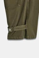 Jeans cargo de tiro medio y corte barrel leg, color verde militar. Presenta bolsillos laterales con solapa en las piernas, bajo ajustable con trabilla y botón, y cierre frontal con cremallera y botón.