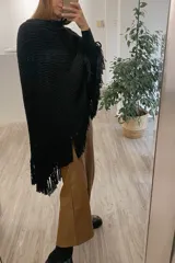 Poncho tejido de lana merino color negro con cuello alto y flecos en el ruedo.