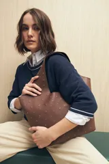 Bolso tipo tote negro de cuero sintético con micro tachas metálicas plateadas. Tiene asas integradas para llevar al hombro.