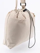 Bolso tipo tote de color beige, con diseño minimalista, cierre superior mediante cordón ajustable y costuras visibles en contraste.