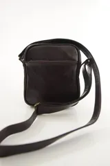 Morral bandolera de cuero genuino color marrón, con diseño compacto, cierre superior y correa ajustable para el hombro.
