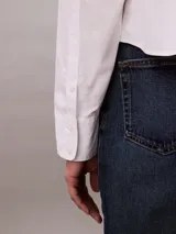 Camisa blanca de algodón y elastano, con cuello clásico de punta, cierre frontal con botones y mangas largas con puños abotonados.