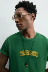 Camiseta de corte relajado, color verde, con cuello redondo y manga corta. Presenta un texto bordado en relieve con letras amarillas y contorno oscuro en el centro del pecho.