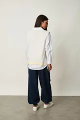 Chaleco de punto color beige claro con escote en V, sin mangas y diseño abierto en los laterales con ajuste de cintas para atar.