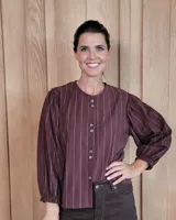 Camisa de manga larga con diseño de rayas verticales y bordados sutiles. Presenta cuello redondo, cierre frontal con botones y mangas abullonadas con volados en los hombros.