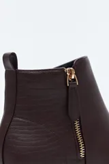 Bota corta de cuero sintético color negro, con taco bajo cuadrado y cierre lateral metálico. Presenta un detalle texturizado tipo reptil en la parte posterior del talón.