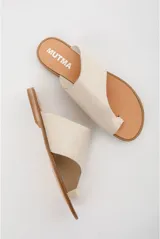 Sandalias chatas de cuero color off-white, con diseño minimalista de tira ancha asimétrica y presilla para el dedo.