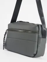 Bandolera de diseño compacto y estilo deportivo, confeccionada en material impermeable color verde. Cuenta con correa ajustable para el hombro, cierre principal y un bolsillo frontal con cierre decorado con tiradores de cordón.