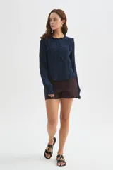Blusa blanca de viscosa con cuello a la base, mangas largas abullonadas con puños ajustados, detalles de volados, encaje y botones frontales.