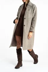 Tapado largo de corte oversize en color beige, con solapas clásicas y cierre frontal con botones. Presenta un diseño minimalista y elegante, ideal para un look sofisticado.