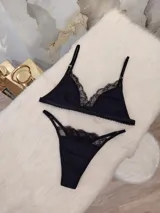 Conjunto de lencería compuesto por un corpiño triangular y una bombacha, ambos confeccionados en algodón negro con detalles de encaje en los bordes. El corpiño cuenta con breteles regulables y la bombacha presenta un diseño con tiras laterales.