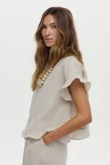 Blusa de lino color beige, de manga corta con volados, cuello redondo y espalda cruzada con volados.