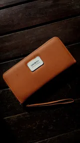 Billetera larga con cierre perimetral, confeccionada en material sintético con estampado botánico de flores silvestres sobre fondo claro. Cuenta con múltiples compartimentos internos para tarjetas, visor para documentos y un bolsillo interno con cierre. Incluye una correa de mano extraíble.