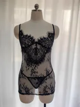Babydoll de encaje negro semitransparente con diseño floral, tirantes finos regulables, escote con costura de realce y espalda descubierta. Incluye una tanga a juego.