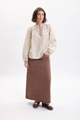 Camisa de manga larga color amarillo pálido con estampa boho a rayas verticales compuestas por pequeños motivos florales. Posee cuello alto con volados y cordones para atar en el frente, y mangas abullonadas con puños ajustados.
