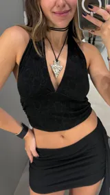 Top negro con acabado brillante, diseño de cuello halter y escote profundo en V. Presenta un ajuste al cuerpo con frunces laterales.
