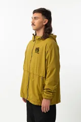 Campera de nylon color mostaza, estilo 'gorpcore', con forro de jersey de algodón y corte confortable. Presenta cierre frontal, capucha y bolsillos laterales. Estampado en el pecho con el logo de la marca y la frase "Release the hounds".