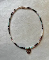 Collar de cuentas facetadas de piedras naturales multicolor con dije dorado ovalado en forma de sol con una piedra central.