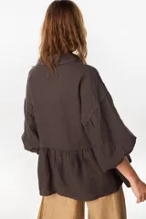 Camisa de lino marrón oscuro con silueta holgada, cuello camisero, cierre frontal de botones claros, mangas voluminosas y detalle de frunces en la cintura.
