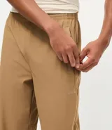 Pantalón deportivo de corte recto, color marrón, con cintura elástica y cordón de ajuste. Presenta bolsillos laterales con cierre y un diseño minimalista de tejido técnico.