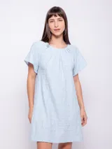 Vestido corto de corte holgado, color celeste, con cuello redondo fruncido y mangas cortas. Está confeccionado en una tela con textura diferenciada que le aporta relieve.