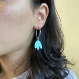 Par de aros plateados de acero quirúrgico hipoalergénico con dije colgante abstracto color naranja.