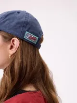 Gorro tipo dad hat de la marca Rusty, color azul con efecto gastado, visera curva y la palabra "RUSTY" bordada en relieve en el frente con letras rojas delineadas en blanco.