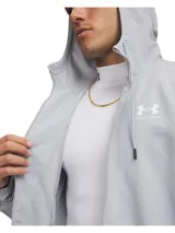 Campera Under Armour tipo cortavientos color gris, con capucha ajustable con cordones, cierre frontal completo y bolsillos laterales con cierre. Incluye forro de malla y puños elásticos.