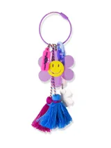 Llavero con aro metálico violeta y dijes colgantes: flor lila con cara sonriente amarilla, flor blanca, borla de hilo azul y borla de hilo fucsia.